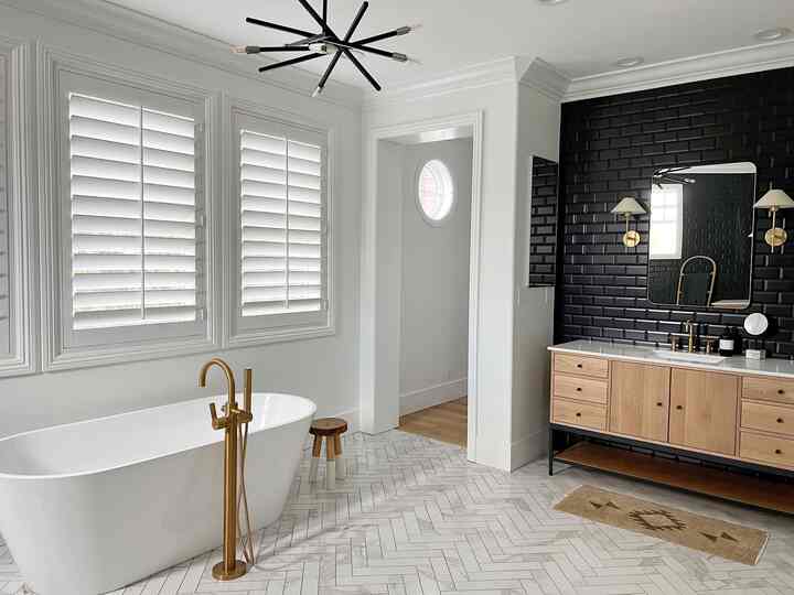 Modern bathroom in white and gold tones featuring a freestanding tub and black tiled accent wall creating a clean look
