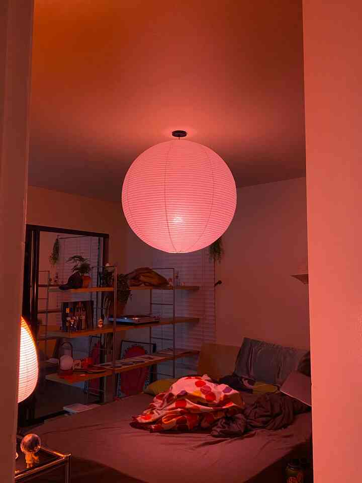 Red-lit bedroom featuring a large spherical pendant light at center ceiling, a bed below, and shelving unit to the left, creating cozy ambiance