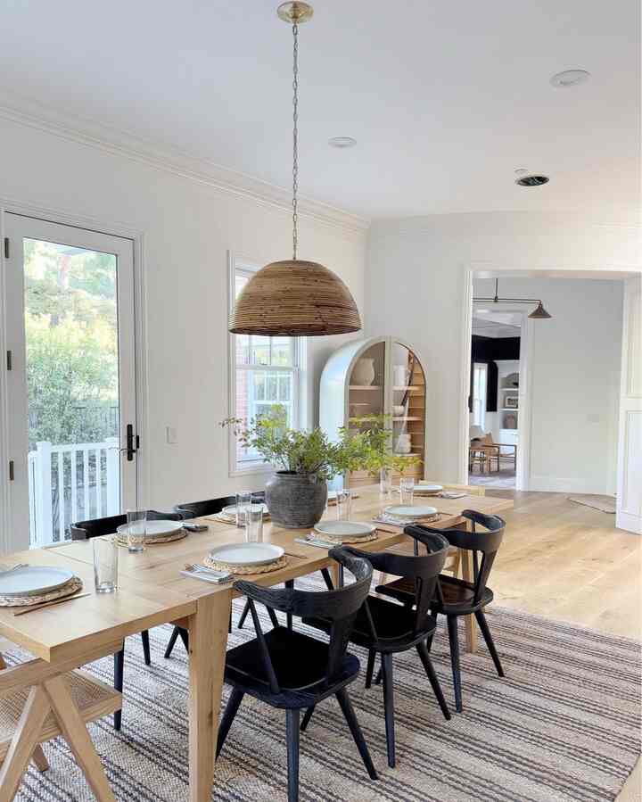 Bright wood tone and white modern dining room featuring black dining chairs and table with stylish setting