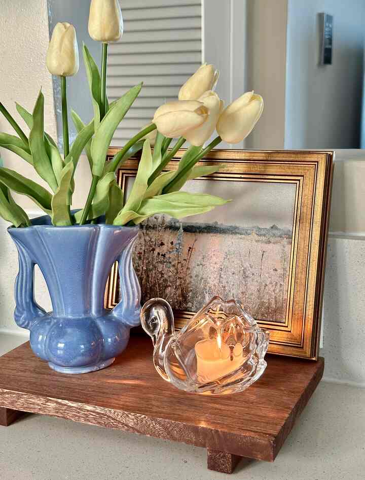 White and blue toned kitchen space featuring a blue vase with artificial tulips, candle, and framed artwork with cozy decorative objects