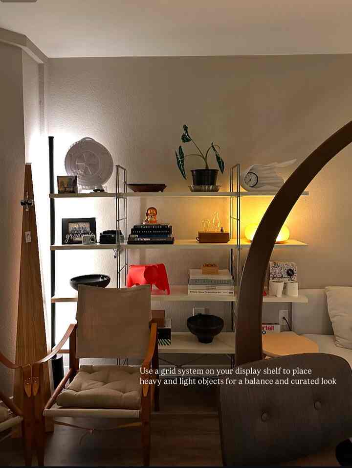 A cozy living room with white walls and wood-tone furniture, featuring shelves and armchairs creating a warm atmosphere