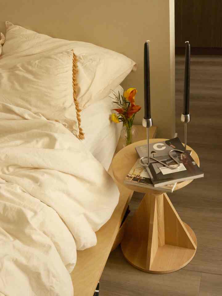 Beige and natural wood-toned bedroom featuring a wooden side table next to the bed with candlesticks and books, creating a cozy atmosphere