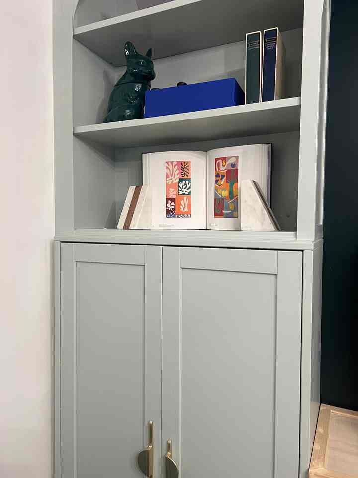 Light grayish white-toned bookshelf with gold handles featuring neatly arranged books and marble bookends in a modern interior