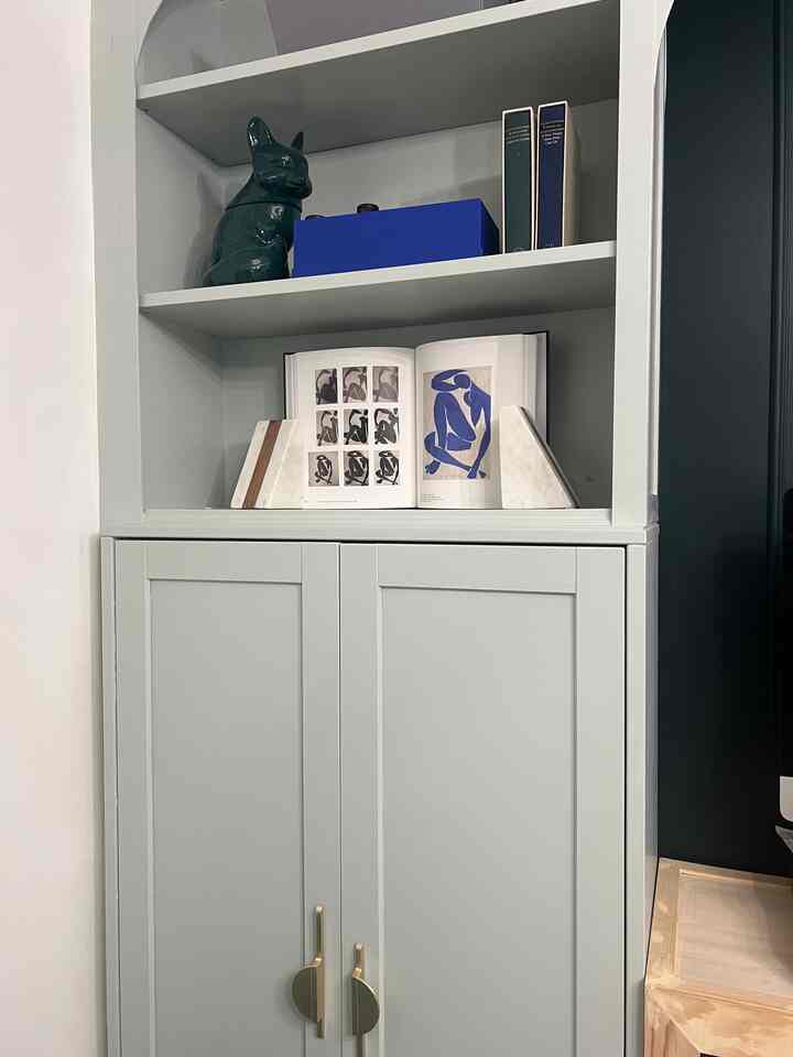 Light gray storage cabinet and bookshelf featuring blue decorative items and books on upper shelves in a modern interior space