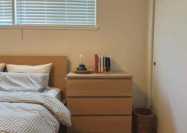 Beige walls and natural wood-tone furniture in a bedroom featuring checkered bedding, chest of drawers, and table lamp creating cozy atmosphere