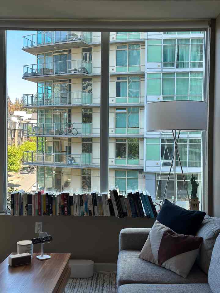 A blue and gray toned living room featuring books curated on the window sill, a Mid-Century Modern floor lamp, and a gray sofa creating a cozy atmosphere