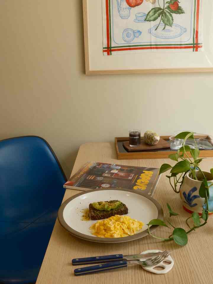 Beige-toned wall and wooden dining table with a blue chair in a modern dining space featuring a plate with avocado toast and scrambled eggs