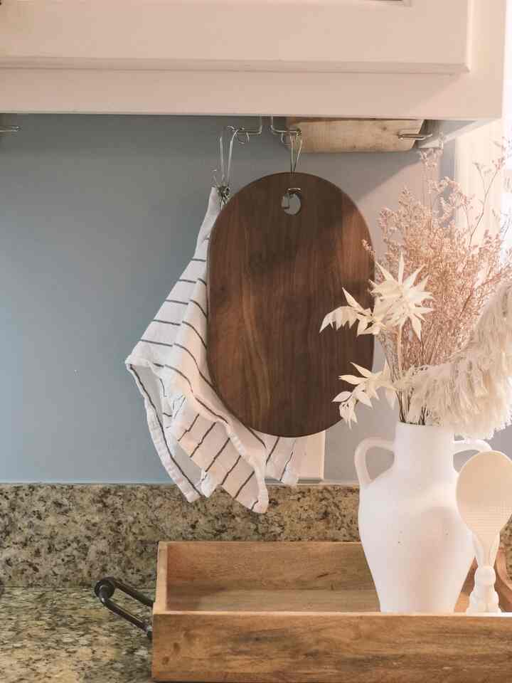 Natural color and white toned kitchen space featuring a cutting board and kitchen towel hanging, creating a cozy storage idea area