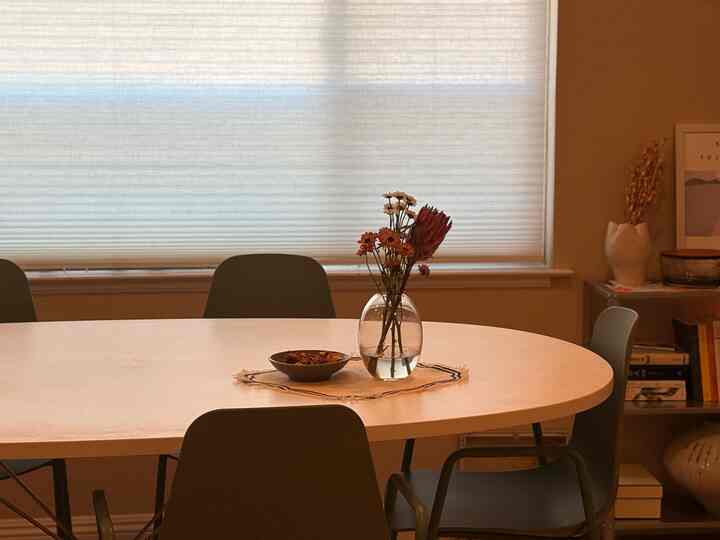 Natural-toned dining room with warm beige walls, white oval dining table, and dark green dining chairs arranged around it