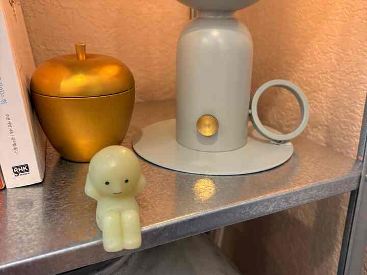 Cozy display on metal-toned shelf featuring a table lamp, golden apple objet, and a small figure figurine