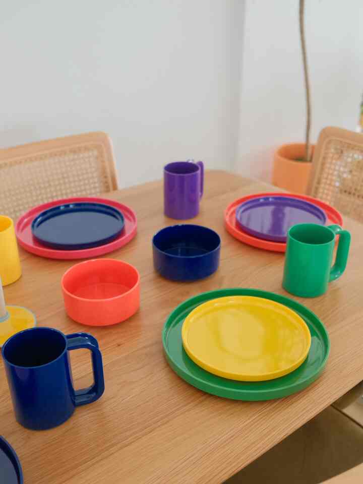 Colorful plates and mugs arranged on a simple wooden dining room table setting