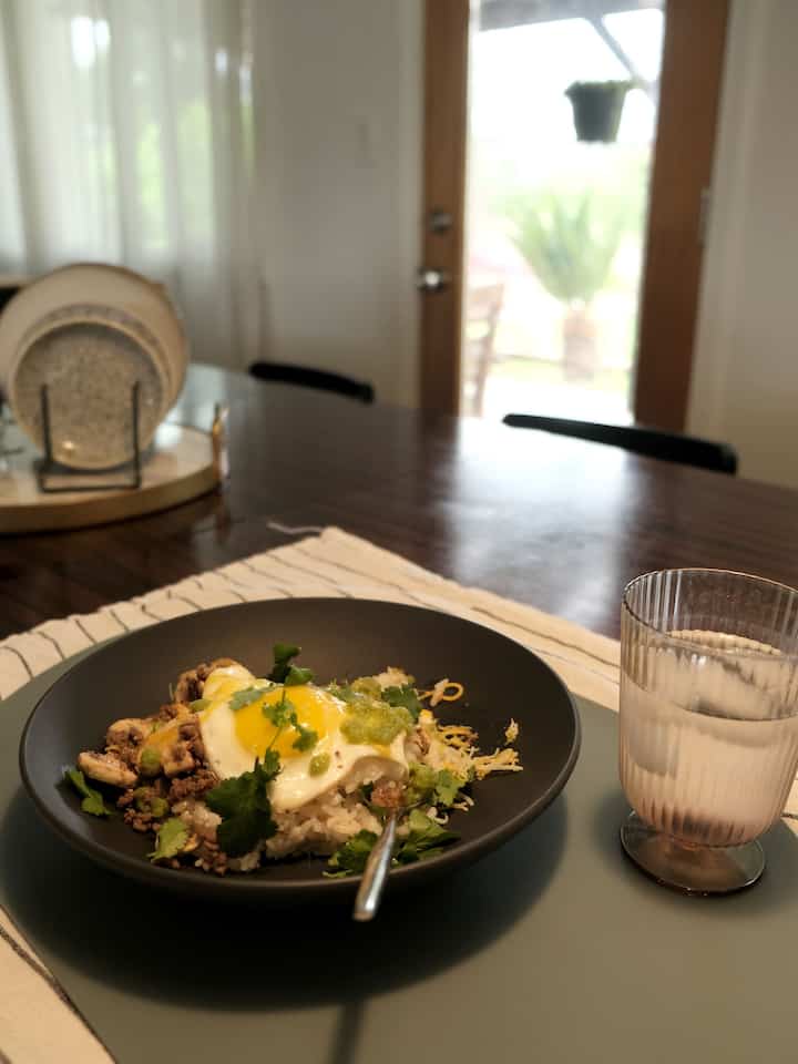 Bright white walls and wood-tone dining table in a dining room, featuring a bowl and glass on a placemat conveying a cozy breakfast mood