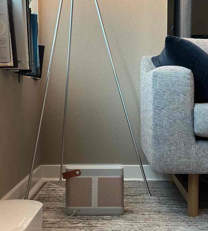 Gray sofa and mid-century modern floor lamp in white-walled living room corner featuring a Bluetooth speaker