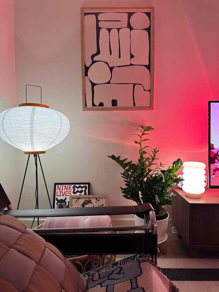A living room with white and red tones featuring a floor lamp, leather armchair, plant, and abstract wall art creating a cozy atmosphere
