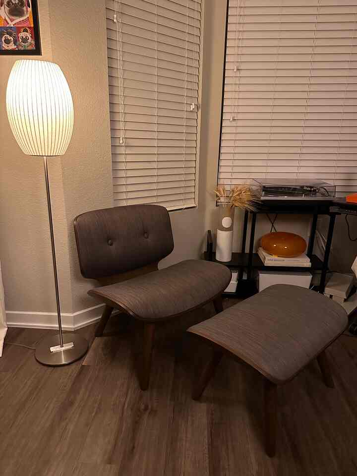 Wood-toned brown Mid-Century Modern living room corner featuring a comfortable armchair with ottoman and warm floor lamp for a cozy atmosphere