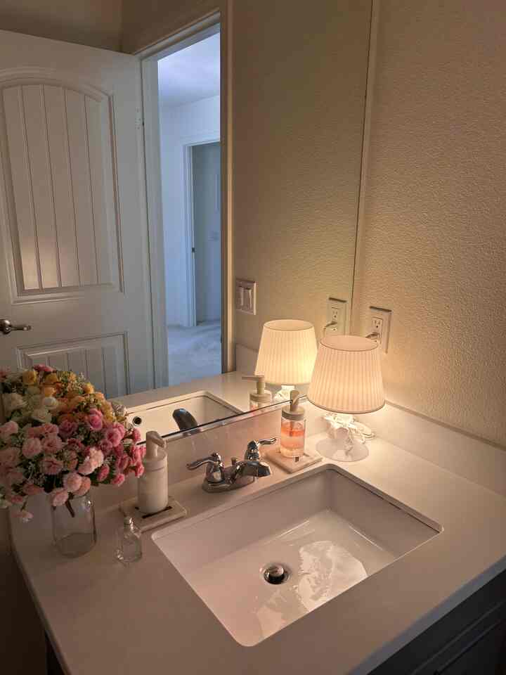 White-toned powder room featuring a sink, mirror, table lamp, and vase creating a cozy atmosphere