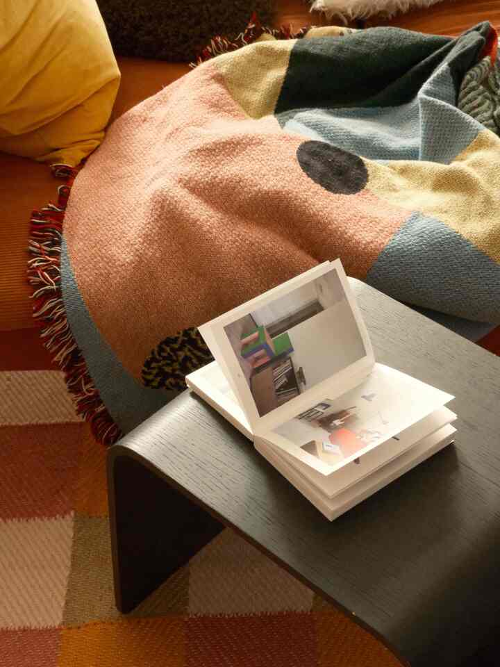 A cozy living room with soft beige and orange tones, featuring a colorful blanket draped over furniture and a dark coffee table with an open book