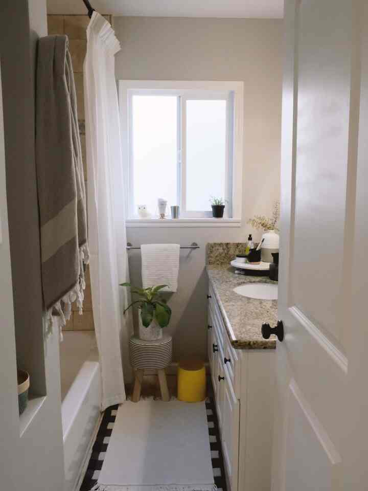 Soft neutral-tone bathroom with white curtains, green plants, and compact fixtures creating a cozy and calming space