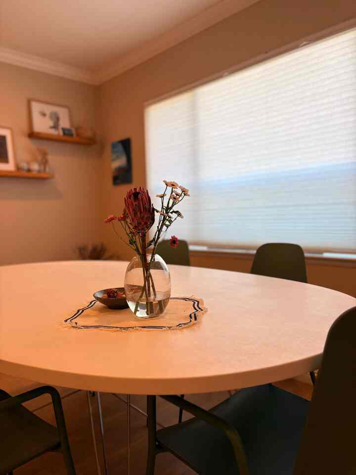 Natural light-toned dining room featuring a white oval dining table surrounded by four dining chairs and a central flower vase, creating a cozy atmosphere