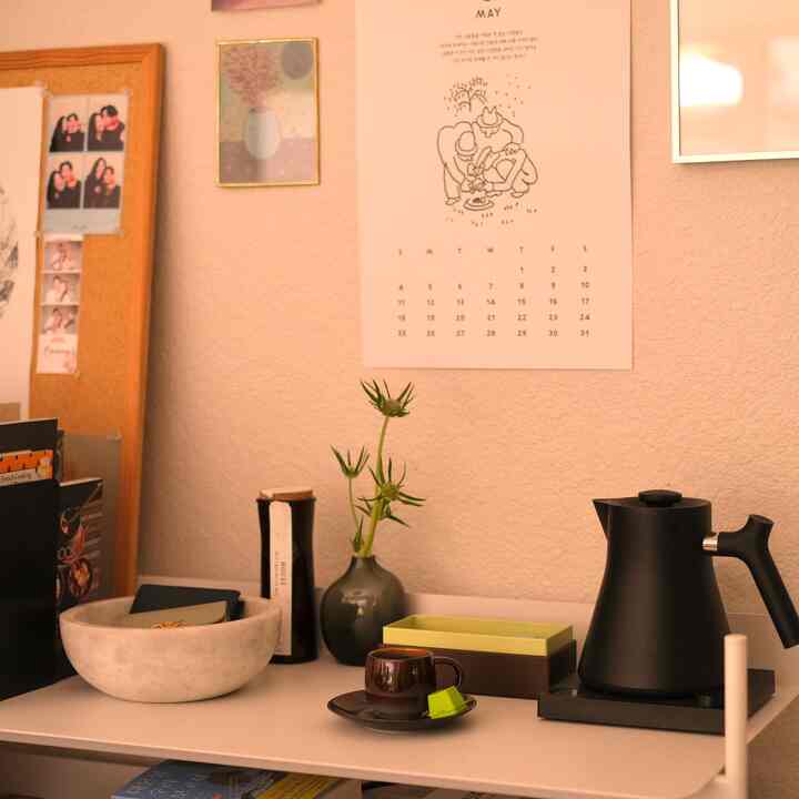 Beige-toned wall with a simple home cafe setup featuring a black electric drip kettle and a marble bowl on a clean kitchen counter