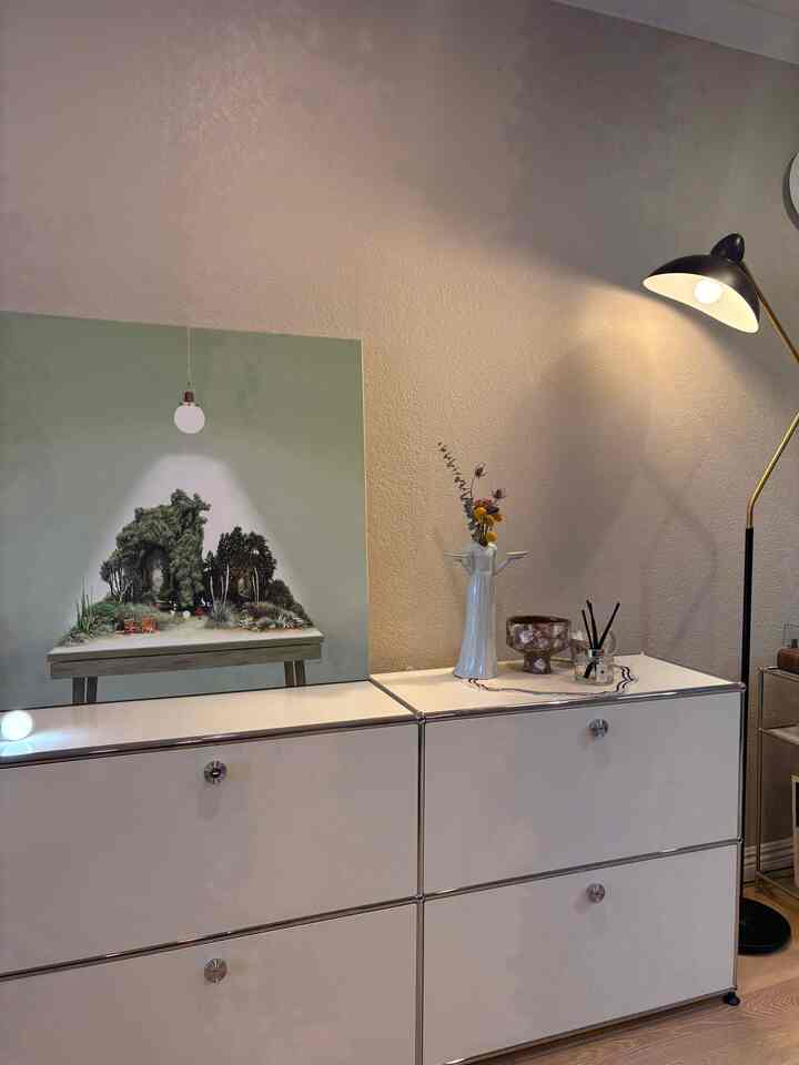 Minimalist living room in white and beige tones featuring sideboard, floor lamp, art, and diffuser with clean decor