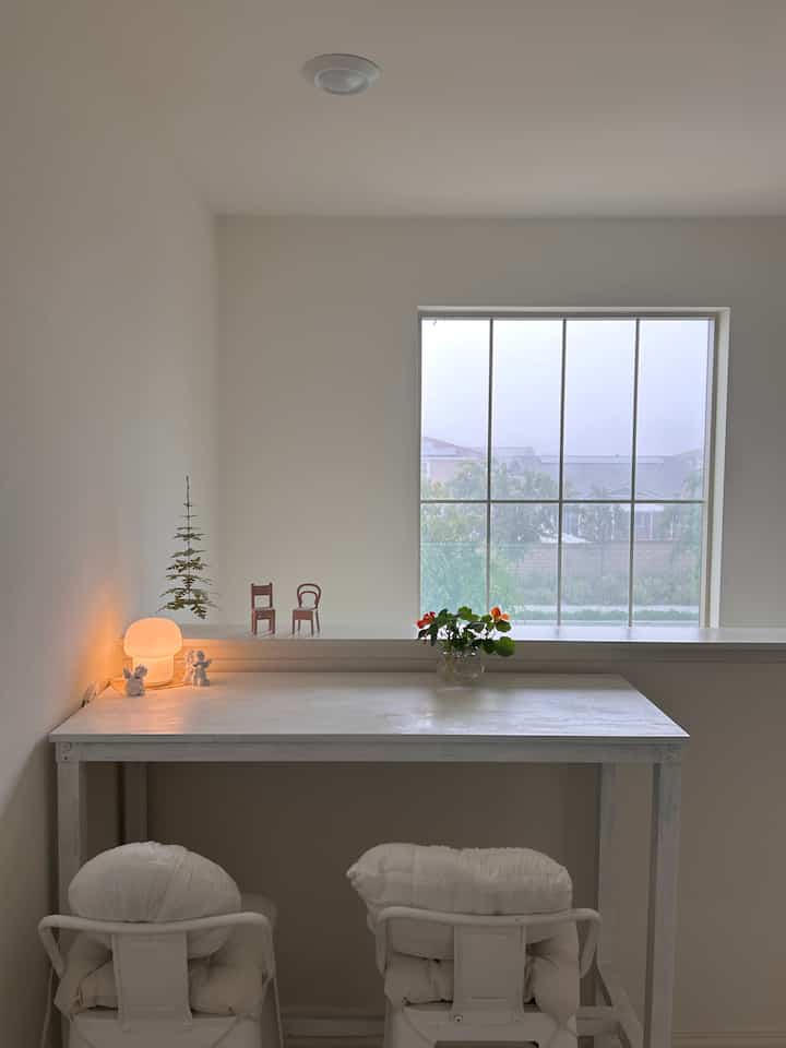 White tone dining room featuring a simple table and chairs with a small plant and lamp, creating a clean and open atmosphere