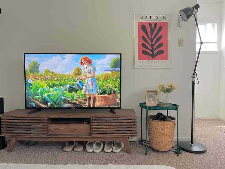 Natural brown wood tone furniture and white walls in living room featuring TV and floor lamp with cozy atmosphere