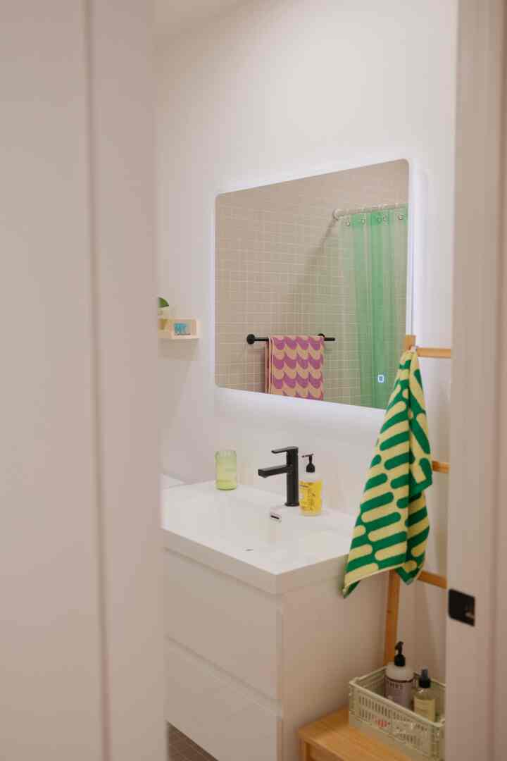 A white-toned bathroom featuring a sleek sink vanity with backlit mirror and a green towel adding a pop of color, showcasing modern design