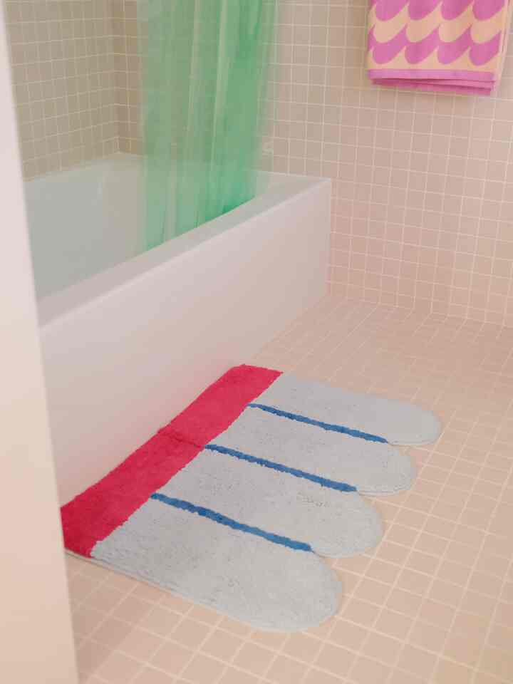 Bright bathroom with pink tiled walls and floor, white bathtub, and pastel-colored bath mat creating a soft atmosphere