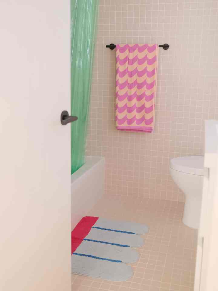 White and beige tiled bathroom featuring a pink towel and green shower curtain with a cozy atmosphere