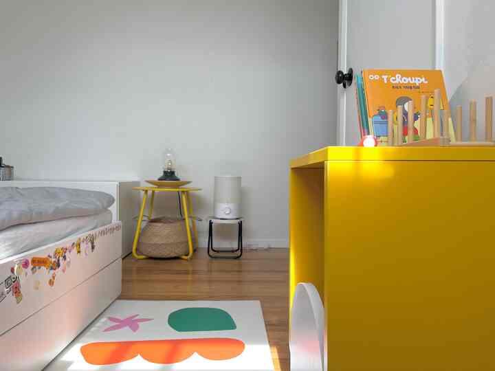 Kids' room with white walls and yellow furniture, natural wood flooring and charming accessories creating a bright space