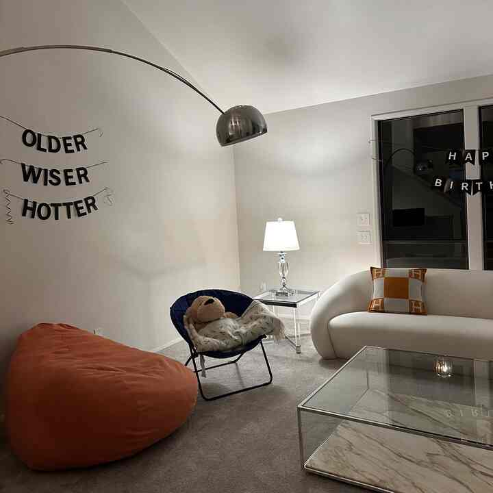 White and gray toned studio living room featuring a curved sofa and orange bean bag in a simple setting