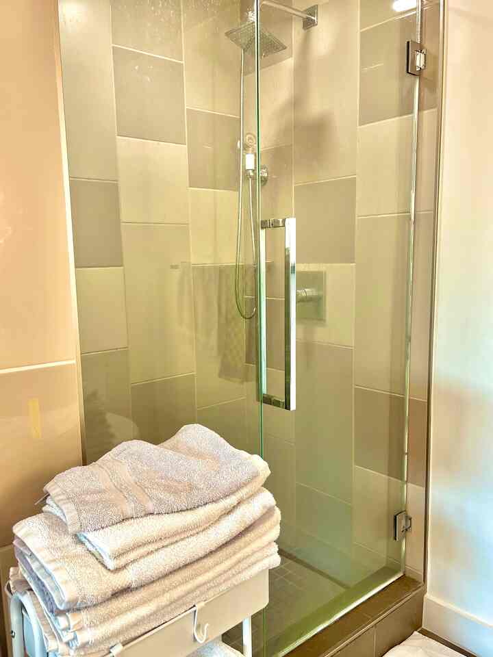 White and beige toned bathroom featuring a glass shower enclosure and neatly stacked towels on a cart