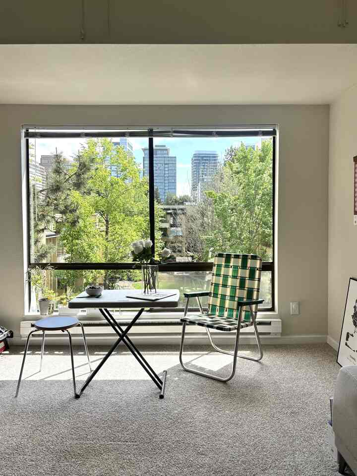Natural-toned living room with white walls and carpet featuring green chair and folding table by a large window