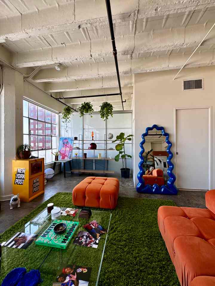 A natural-colored living room featuring vivid orange sofa and ottoman, green rug, and blue wavy mirror for stylish accents