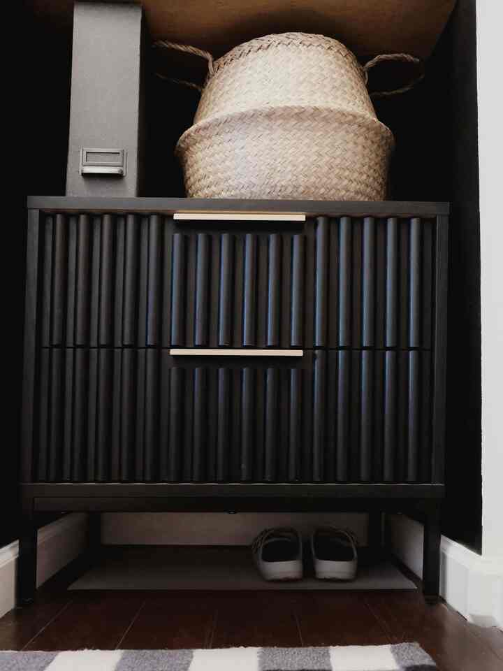Black shoe cabinet located at entrance with natural woven basket on top creating a neat storage space