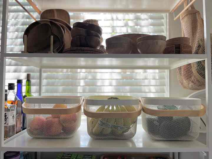 White shelving with beige-toned bamboo serving bowls and organized storage baskets in kitchen space