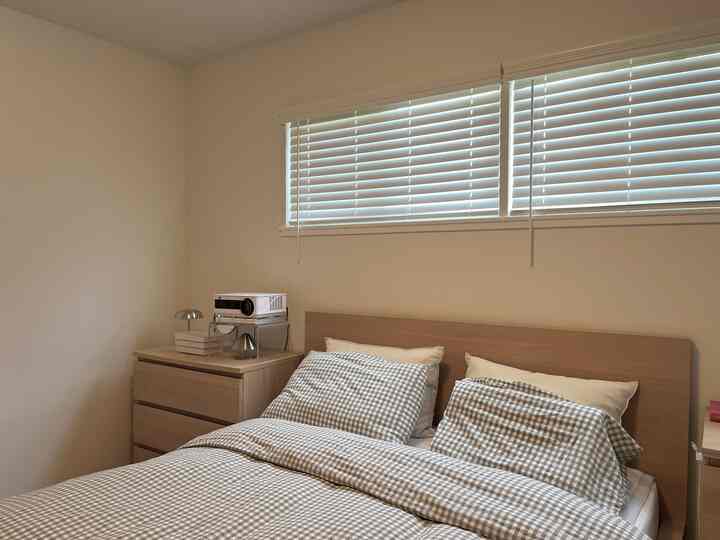 Compact bedroom with white walls and blinds, wood tone bed frame and dresser, featuring gray gingham duvet cover creating a clean atmosphere