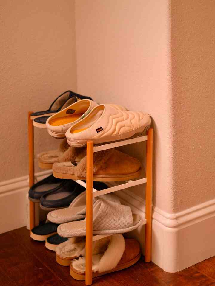 A narrow corner featuring a 3-tier shoe rack in soft beige and wood tones, creating a simple storage space