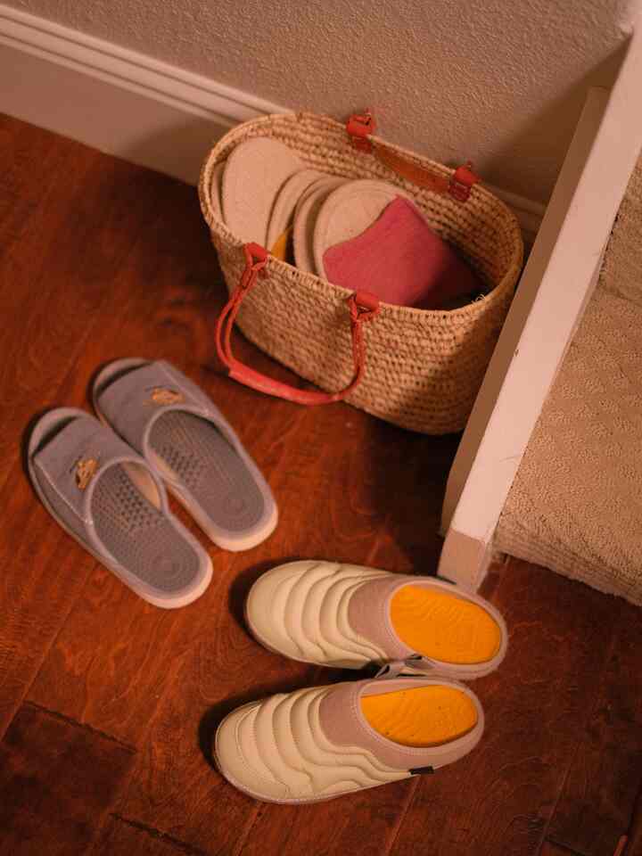 Warm wood tone floor entrance featuring two styles of indoor slippers and a natural woven basket creating a cozy space