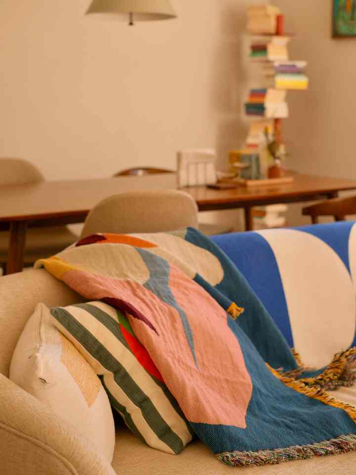 Beige and blue toned living and dining area featuring colorful throws and wooden furniture with a warm atmosphere