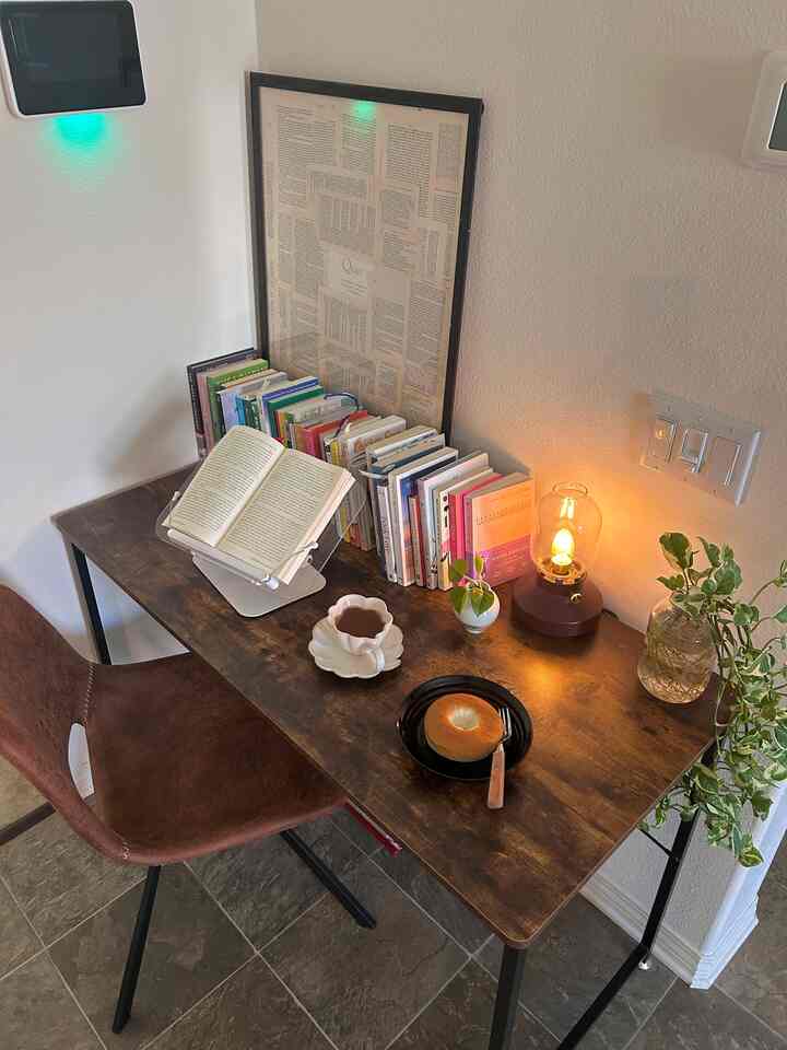 Natural color corner in living room featuring desk with books, coffee cup, and warm table lamp creating cozy atmosphere