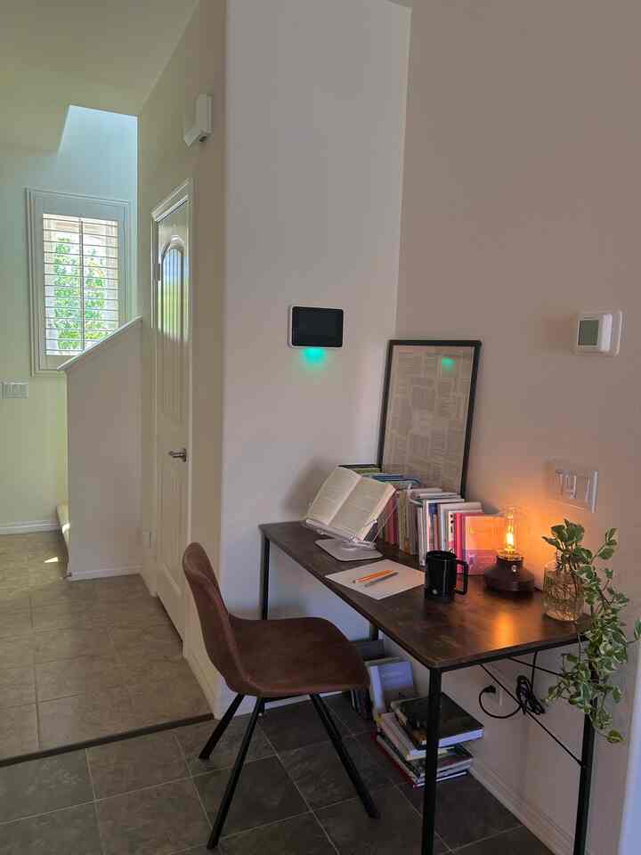 Bright white-walled corner study space featuring a dark brown desk, books, and warm lighting creating a cozy atmosphere