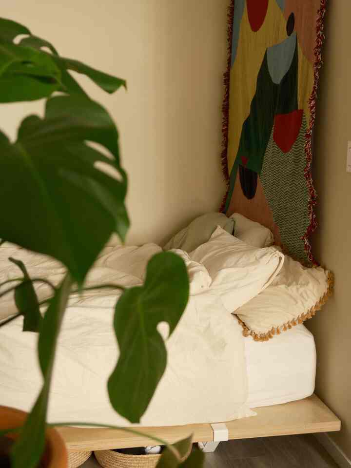 Beige and white toned bedroom corner featuring wooden bed frame and plant in a cozy setting