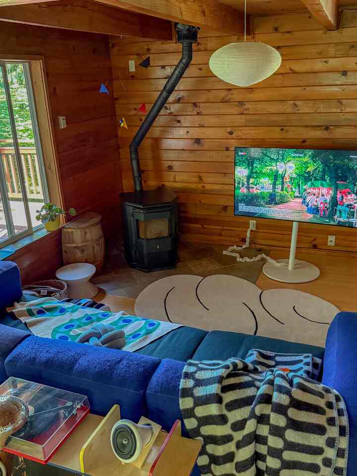 Warm brown wood-toned living room featuring navy sectional sofa and black wood stove with cozy natural atmosphere