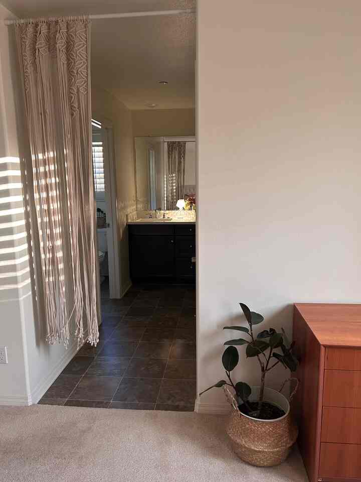 Natural-tone entrance space featuring macrame curtain, woven plant basket, and a bathroom visible through doorway, creating a warm atmosphere