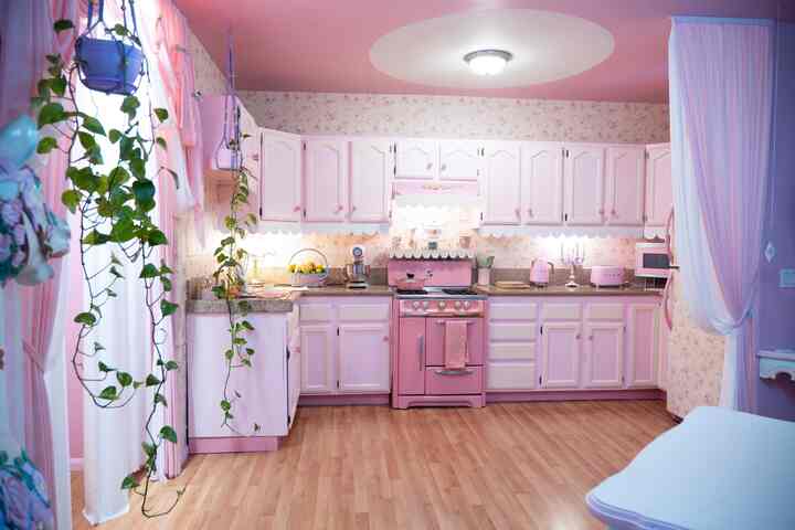 Pink retro kitchen space featuring pastel cabinetry, vintage stove, wood-tone flooring, and floral wallpaper accents
