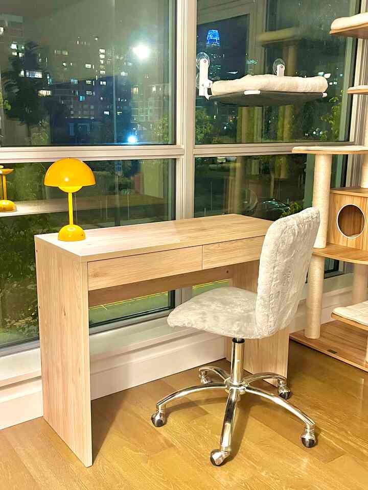 Cozy home office nook with a slim natural wood desk and office chair placed in a corner of the living room featuring wood tones