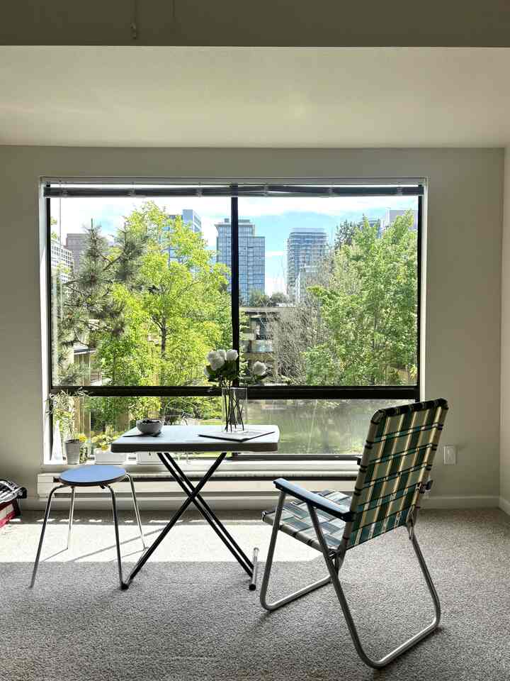 Beige-toned compact room with large window featuring nature view and minimal furniture