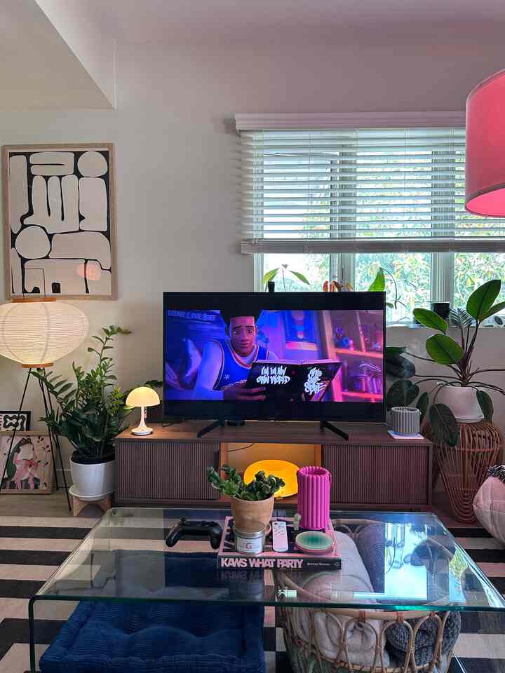 Natural-toned living room featuring a Mid-Century Modern TV stand, plants, and a glass coffee table creating a cozy atmosphere